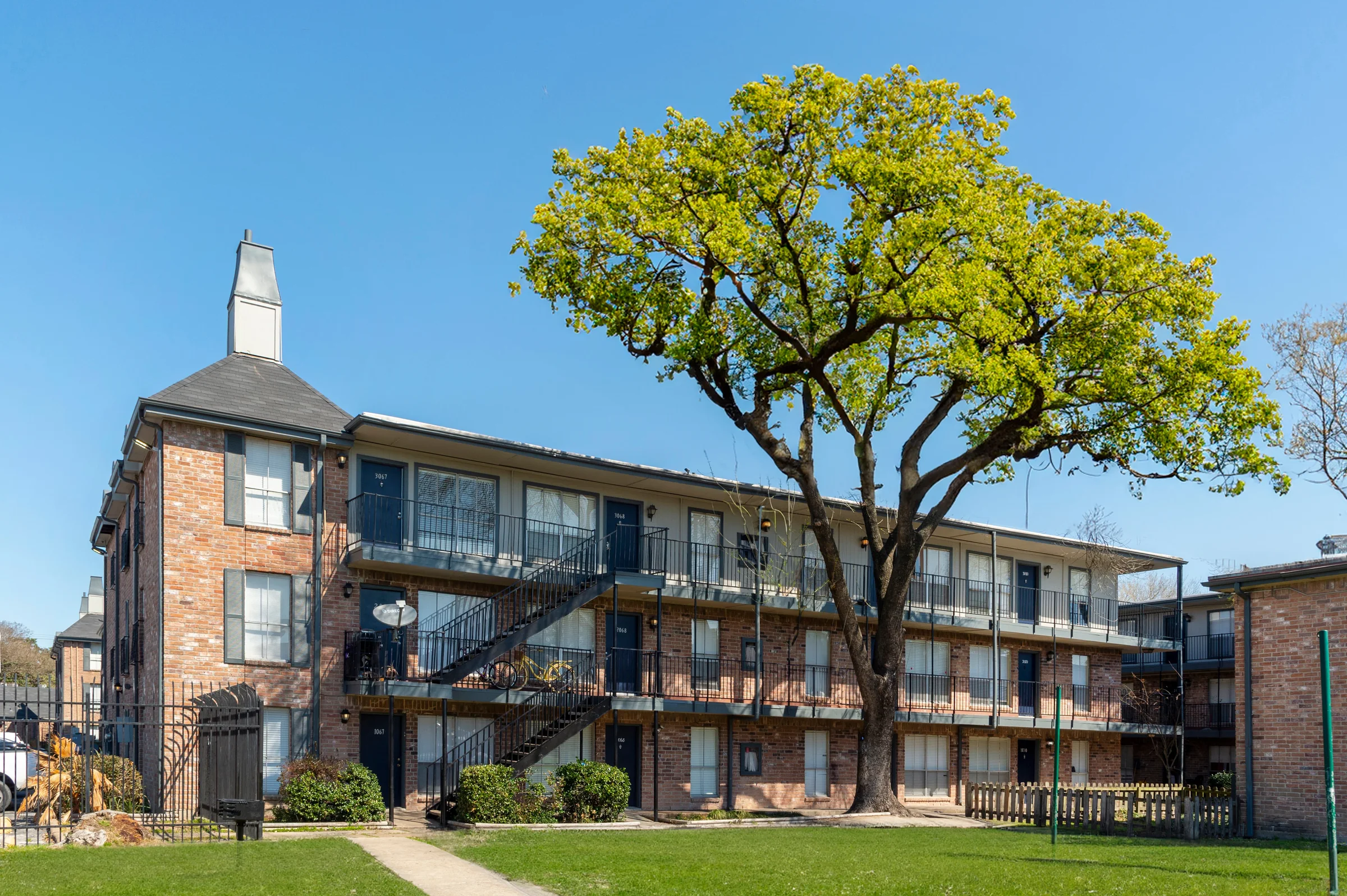Three-story brick building with a mansard roof and balconies under a big live oak at Altair Residences